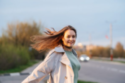 beautiful smiling girl with long hair in the street with a car driving by in the background